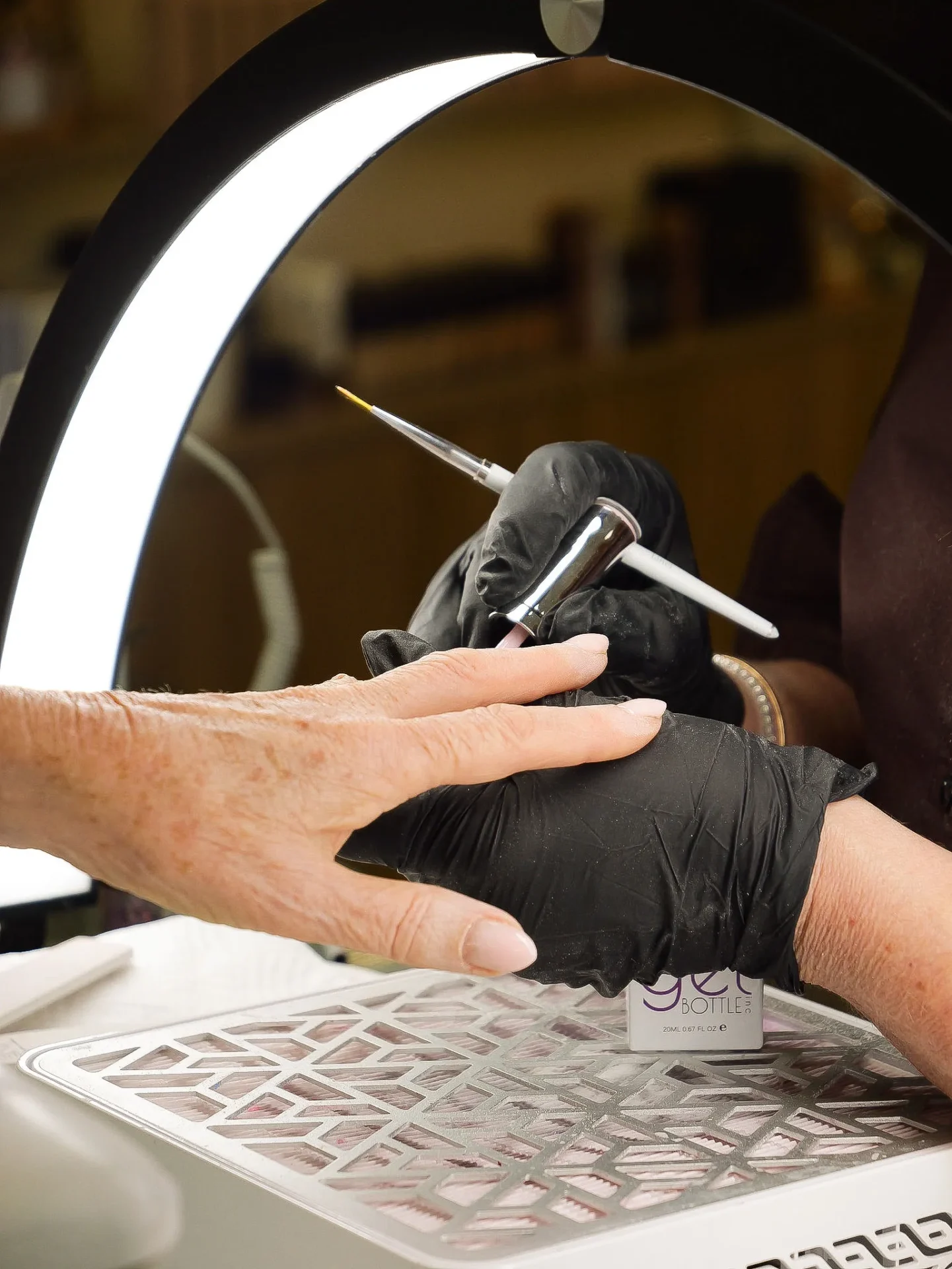 Nail technician airbrushing client's manicure under ring light