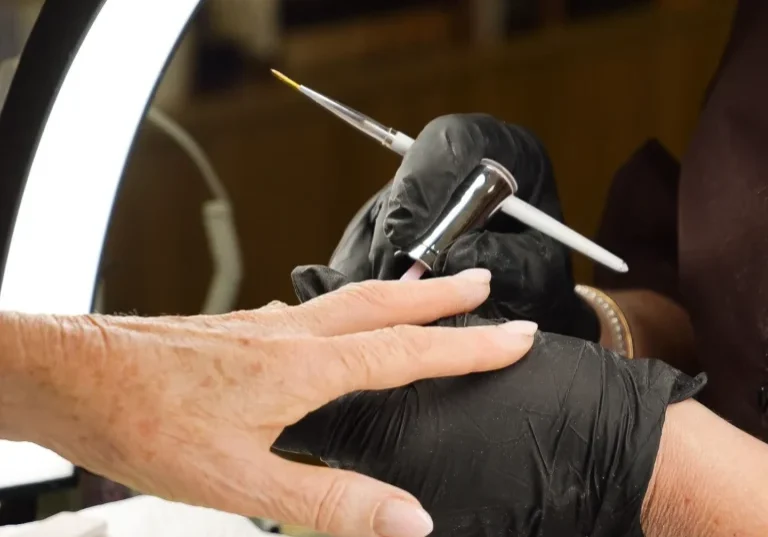Nail technician airbrushing client's manicure under ring light